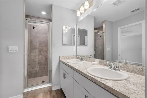 a bathroom with a granite countertop double vanity sink mirror and shower