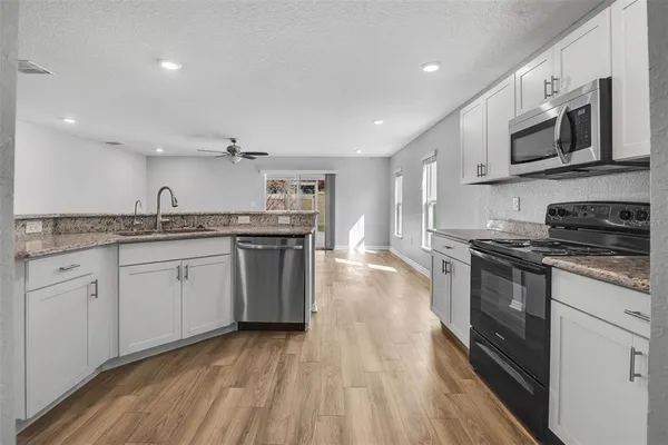 a kitchen with stainless steel appliances granite countertop wooden cabinets a sink a stove a microwave and wooden floors