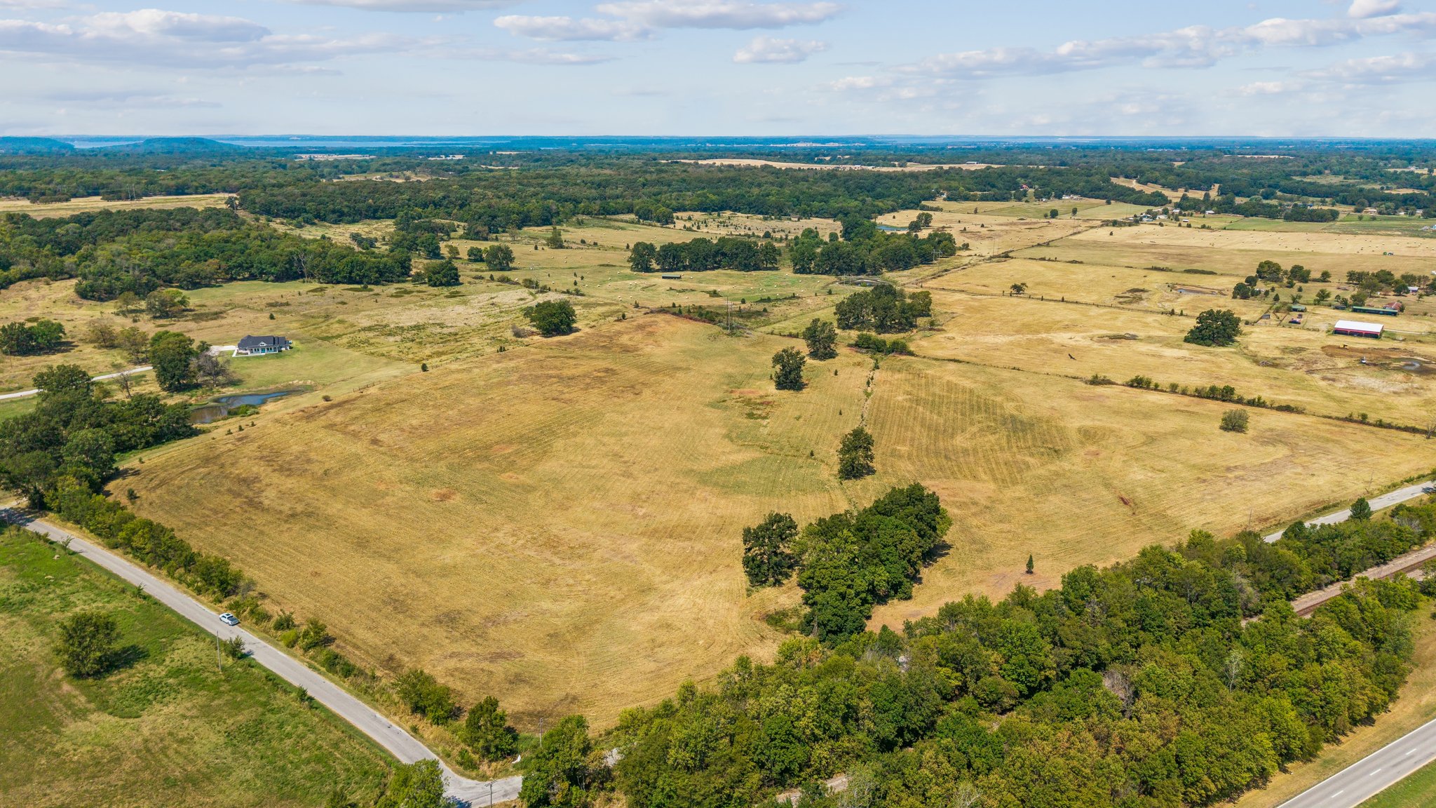 0 4190th Road Claremore, OK 74017 - Photo 2 of 5 Expansive open fields with scattered trees, bordered by a paved road and wooded areas