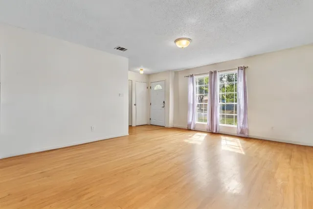 a view of an empty room with wooden floor and windows