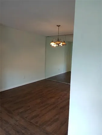an empty room with wooden floor chandelier and kitchen view