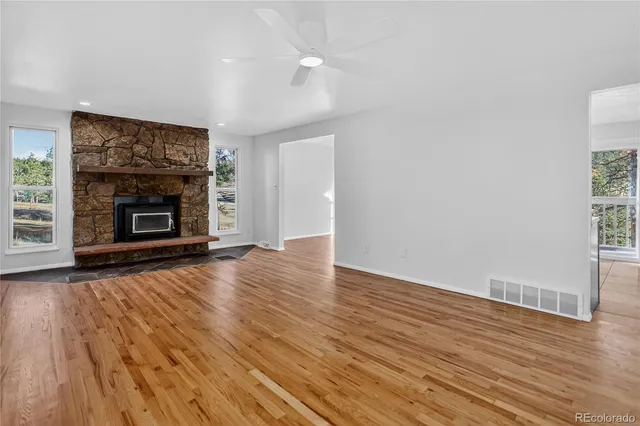 an empty room with wooden floor fireplace and windows