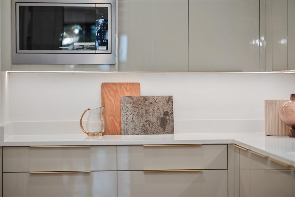 9457 Waterview Road Dallas, TX 75218 - Photo 17 of 25 Sleek kitchen featuring a built-in stainless steel microwave, glossy light gray cabinetry, under-cabinet lighting, and white countertops
