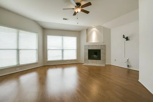 an empty room with wooden floor fireplace and windows