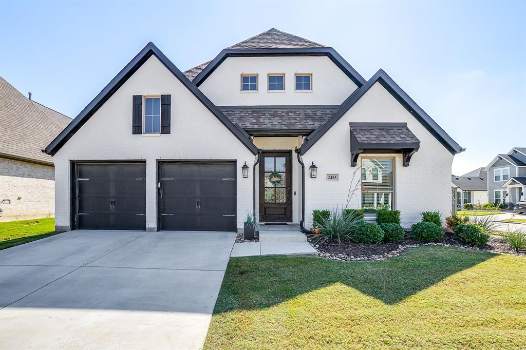 View of front of house with brick siding, a front lawn, concrete driveway, and roof with shingles
