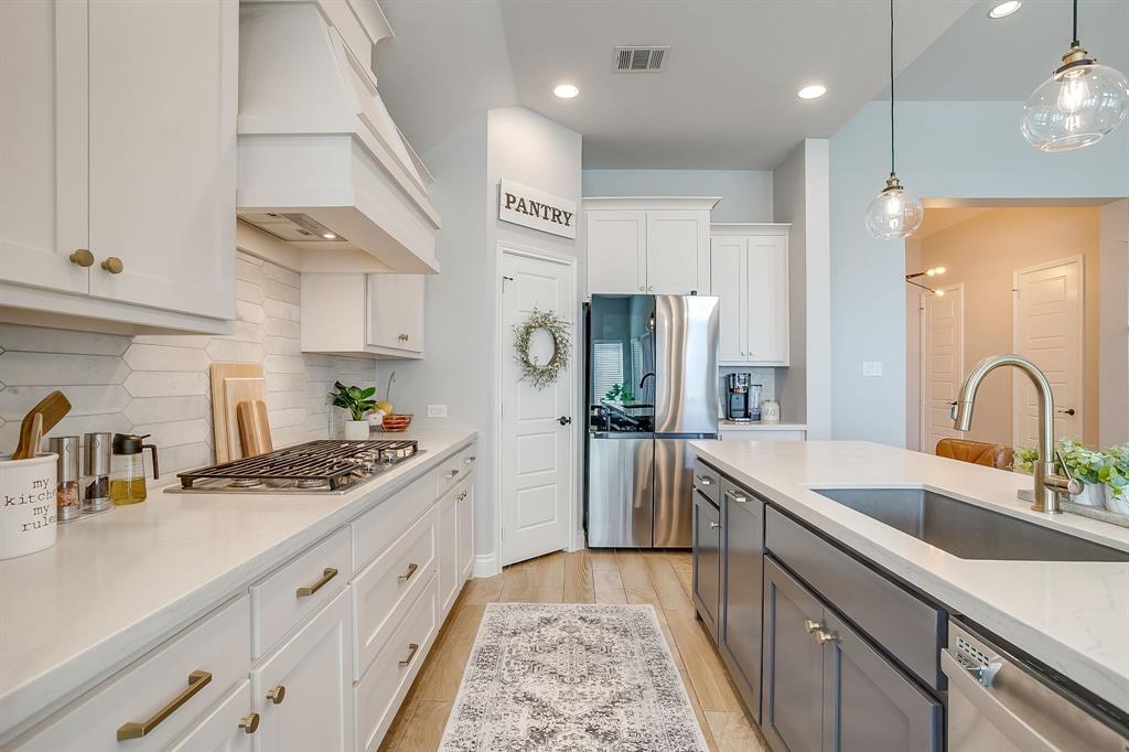 2453 Lazy Dog Lane Northlake, TX 76247 - Photo 11 of 40 Kitchen featuring white cabinets, appliances with stainless steel finishes, light stone counters, hanging light fixtures, and light wood-style floors