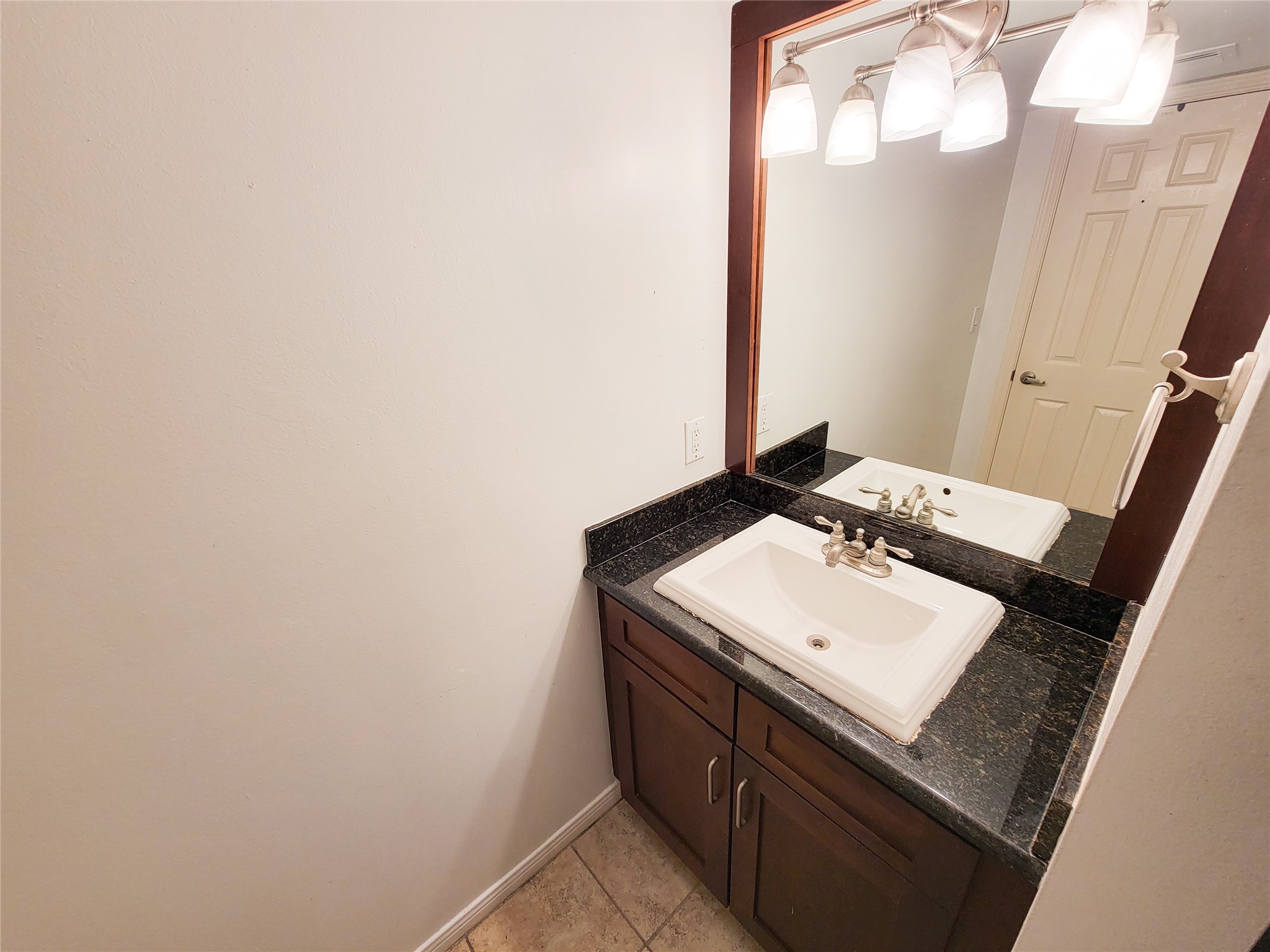3525 Sage Road, Unit 1605 Houston, TX 77056 - Photo 15 of 33 Dark wood vanity features a black granite countertop with decorative overmount sink. Above the vanity is a large mirror with an updated lighting fixture. The room has neutral wall colors and tile flooring.