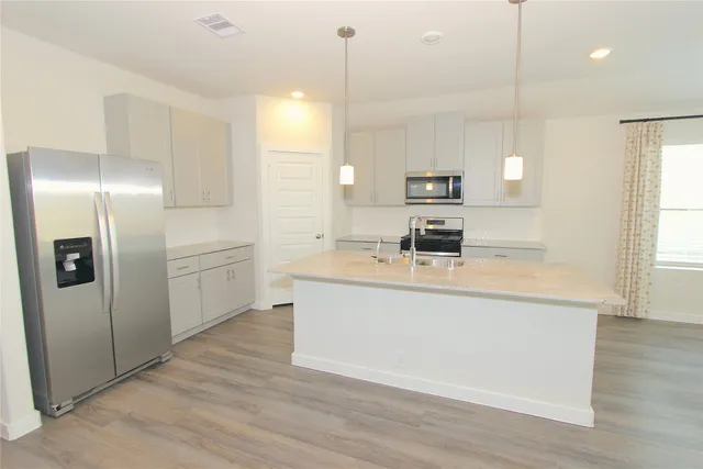 a kitchen with stainless steel appliances granite countertop a sink a stove a refrigerator and white cabinets with wooden floor