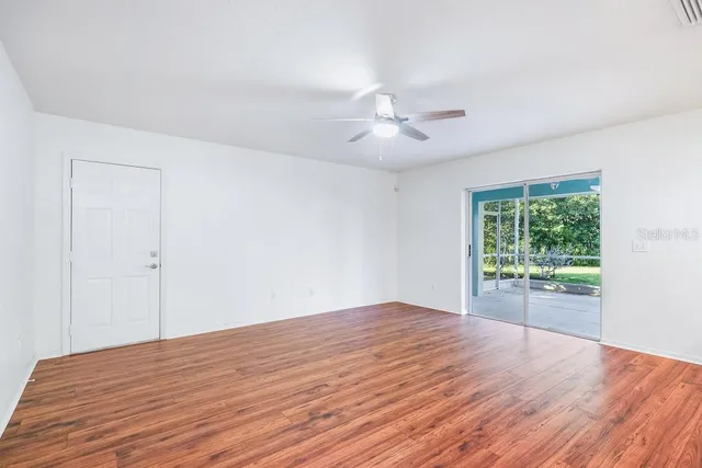 a view of an empty room with wooden floor and a ceiling fan