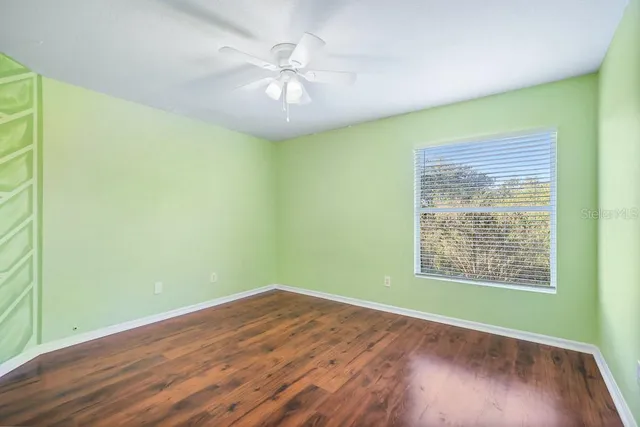 an empty room with wooden floor chandelier fan and windows