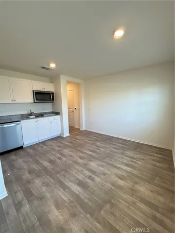 a view of an empty room and kitchen with microwave