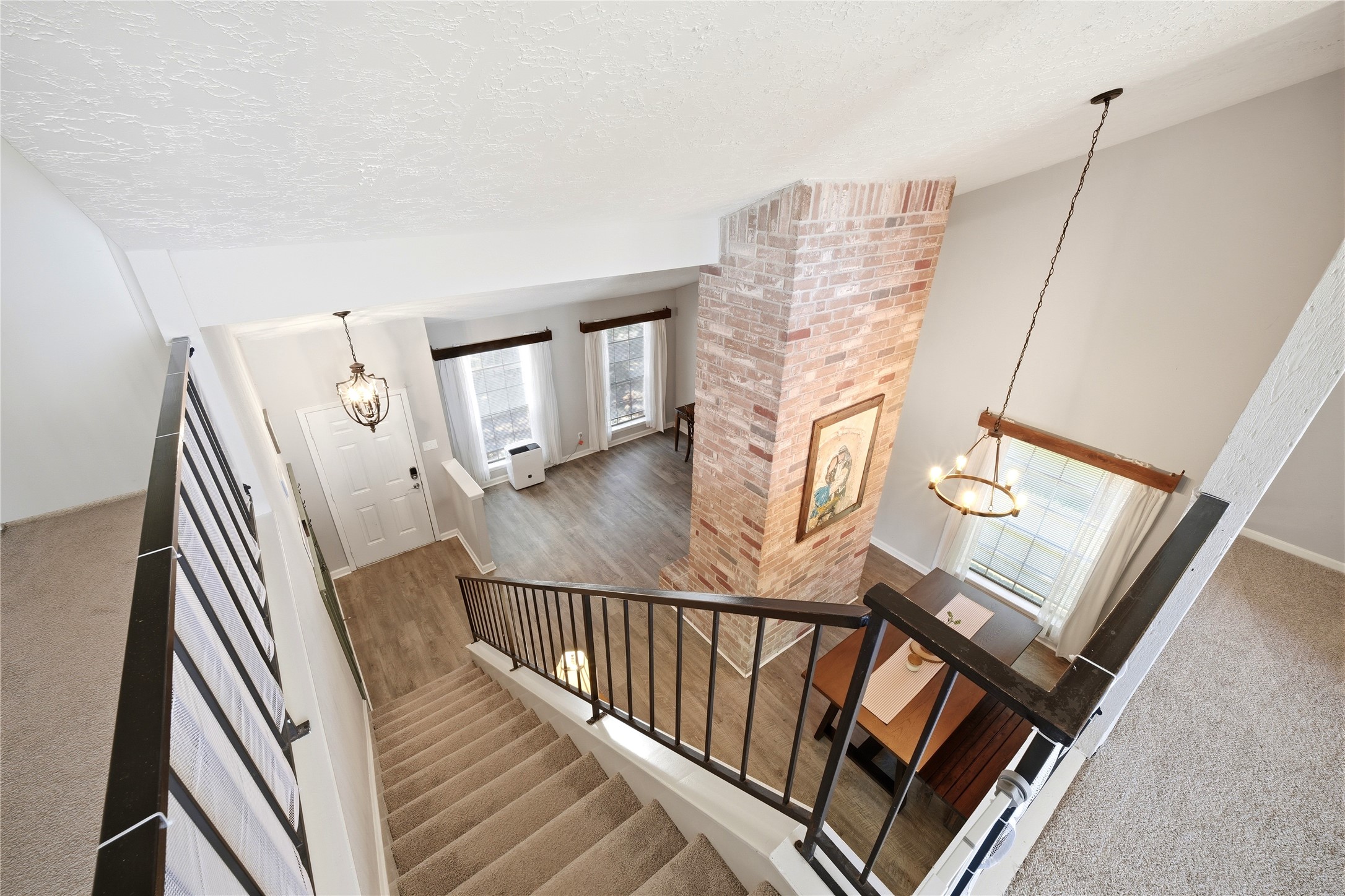 4718 Temple Bell Drive Spring, TX 77388 - Photo 26 of 50 This photo showcases a bright, open-concept living space with a high ceiling, featuring a central brick column. It has a modern staircase with black railings, wood flooring, and large windows that provide ample natural light. The layout includes a dining area and a cozy atmosphere.