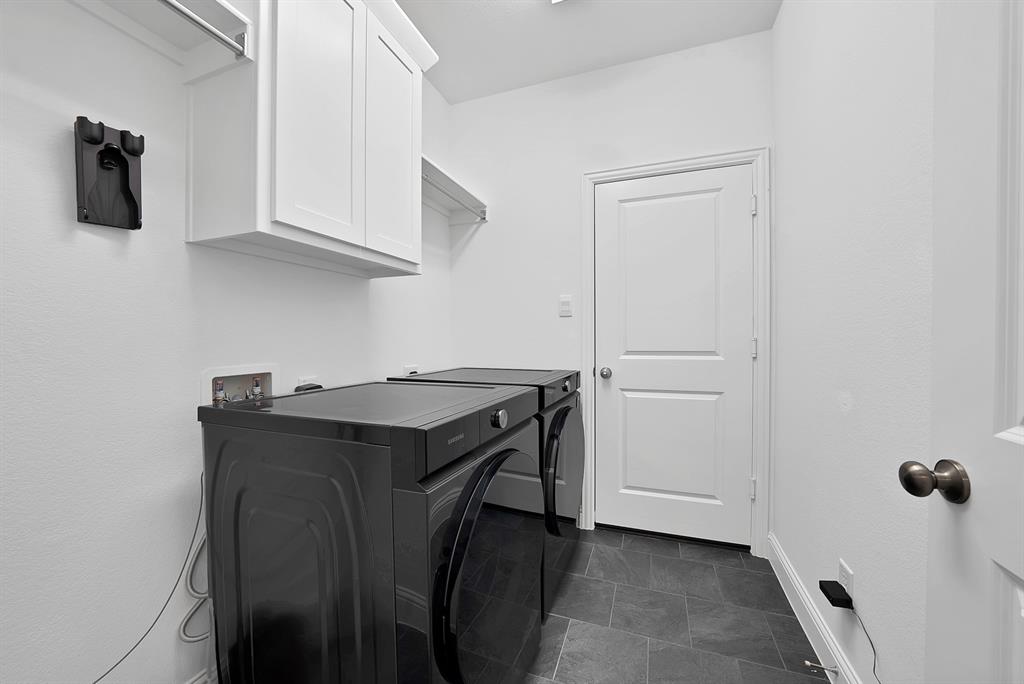 5012 Triadic Lane Prosper, TX 75078 - Photo 32 of 38 Laundry room featuring dark gray tile flooring, crisp white walls, white shaker-style cabinetry, and a wall-mounted shelving unit