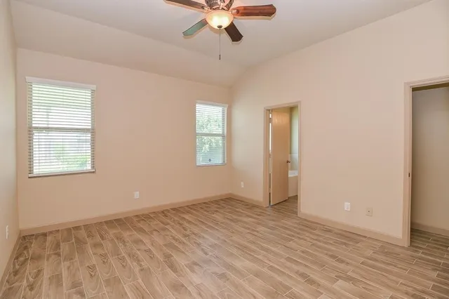 an empty room with wooden floor chandelier fan and windows