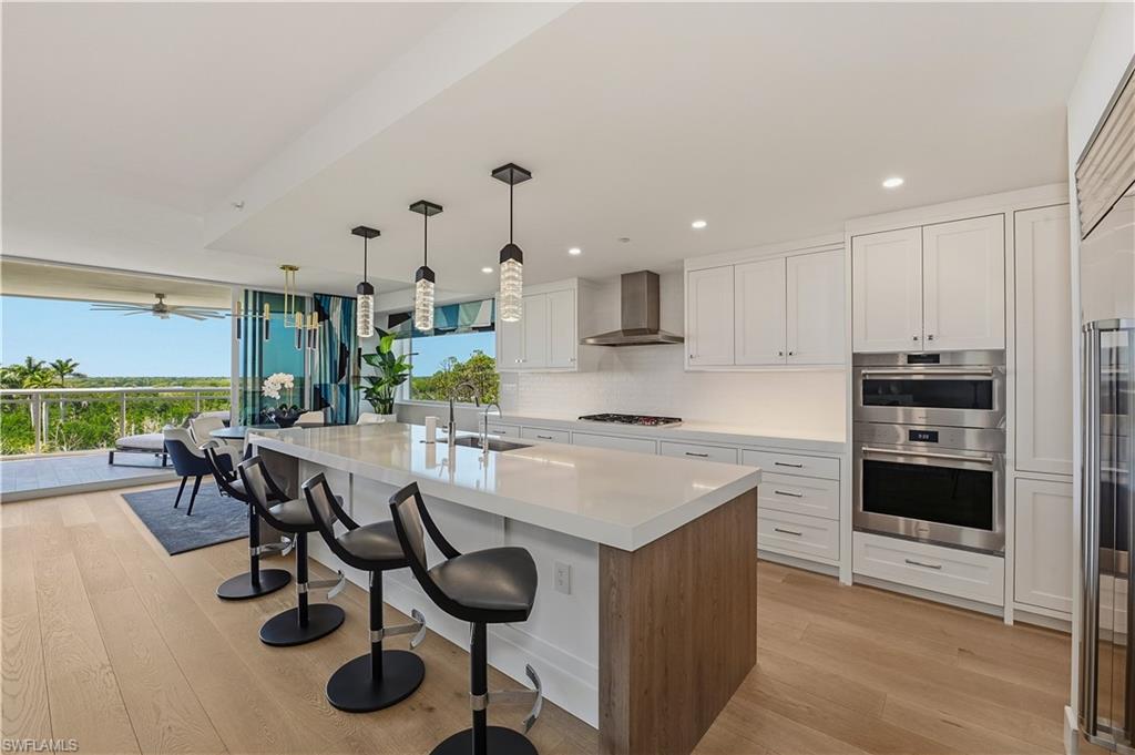 13935 Old Coast Road, Unit 406 Naples, FL 34110 - Photo 2 of 49 Kitchen with a breakfast bar area, an island with sink, light wood-style floors, stainless steel appliances, and dual tone cabinetry
