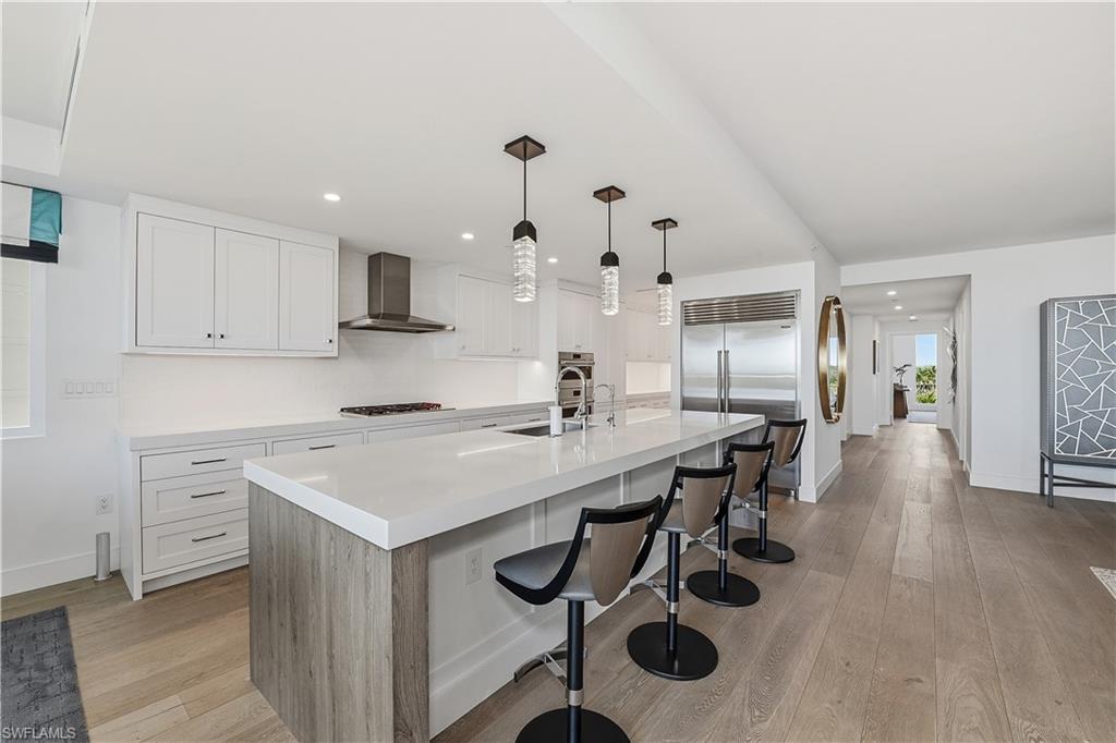13935 Old Coast Road, Unit 406 Naples, FL 34110 - Photo 3 of 49 Kitchen featuring a breakfast bar area, light wood-type flooring, a center island with sink, white cabinets, and hanging light fixtures