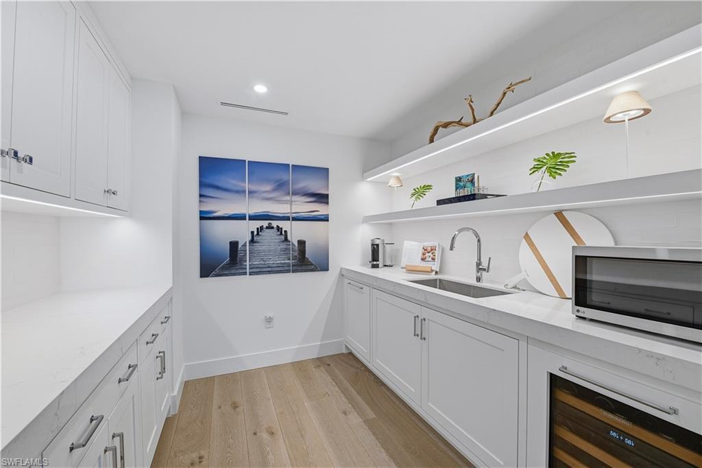 13935 Old Coast Road, Unit 406 Naples, FL 34110 - Photo 4 of 49 Bar area with white cabinets, light wood-style flooring, stainless steel microwave, wine cooler, and open shelves