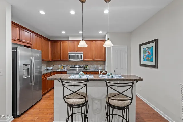 a kitchen with stainless steel appliances granite countertop a refrigerator a sink a stove a dining table and chairs with wooden floor