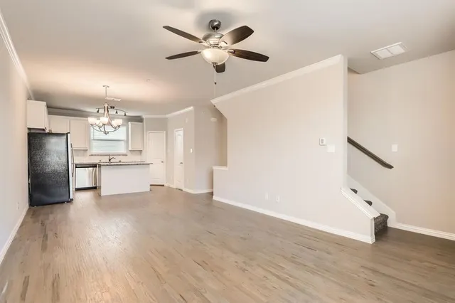 a view of an empty room with wooden floor and a kitchen