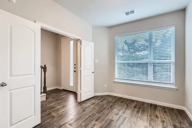 a view of an empty room with wooden floor and a window