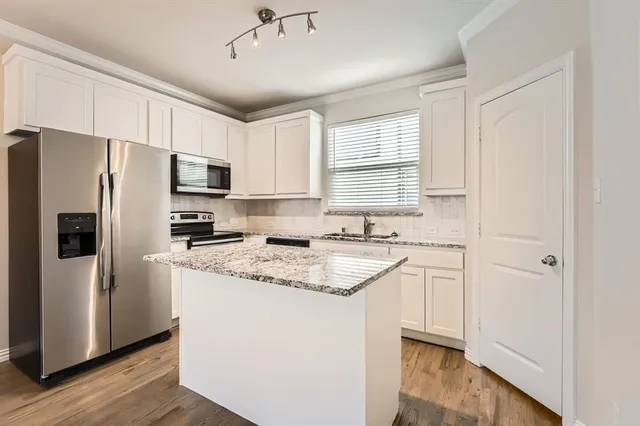 a kitchen with stainless steel appliances granite countertop a refrigerator a sink dishwasher a stove and white countertops with wooden floor