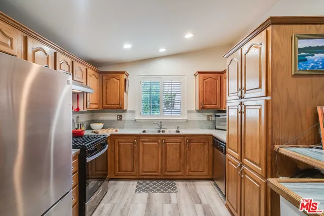 a kitchen with stainless steel appliances granite countertop a refrigerator a sink dishwasher a stove and white countertops with wooden floor