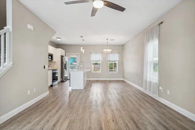 an empty room with wooden floor kitchen view and windows