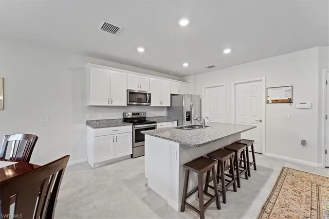 a kitchen with stainless steel appliances kitchen island granite countertop a table chairs sink refrigerator and microwave