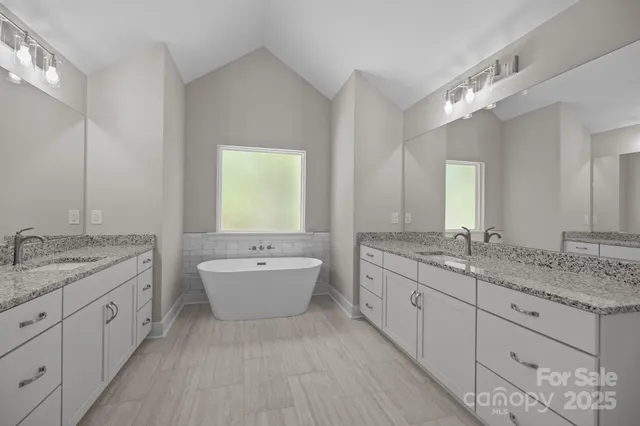 a bathroom with a granite countertop double vanity sink a mirror and a bathtub
