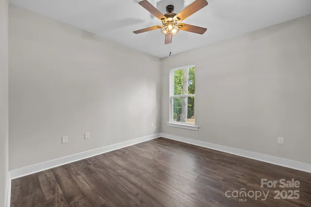 an empty room with wooden floor chandelier fan and windows