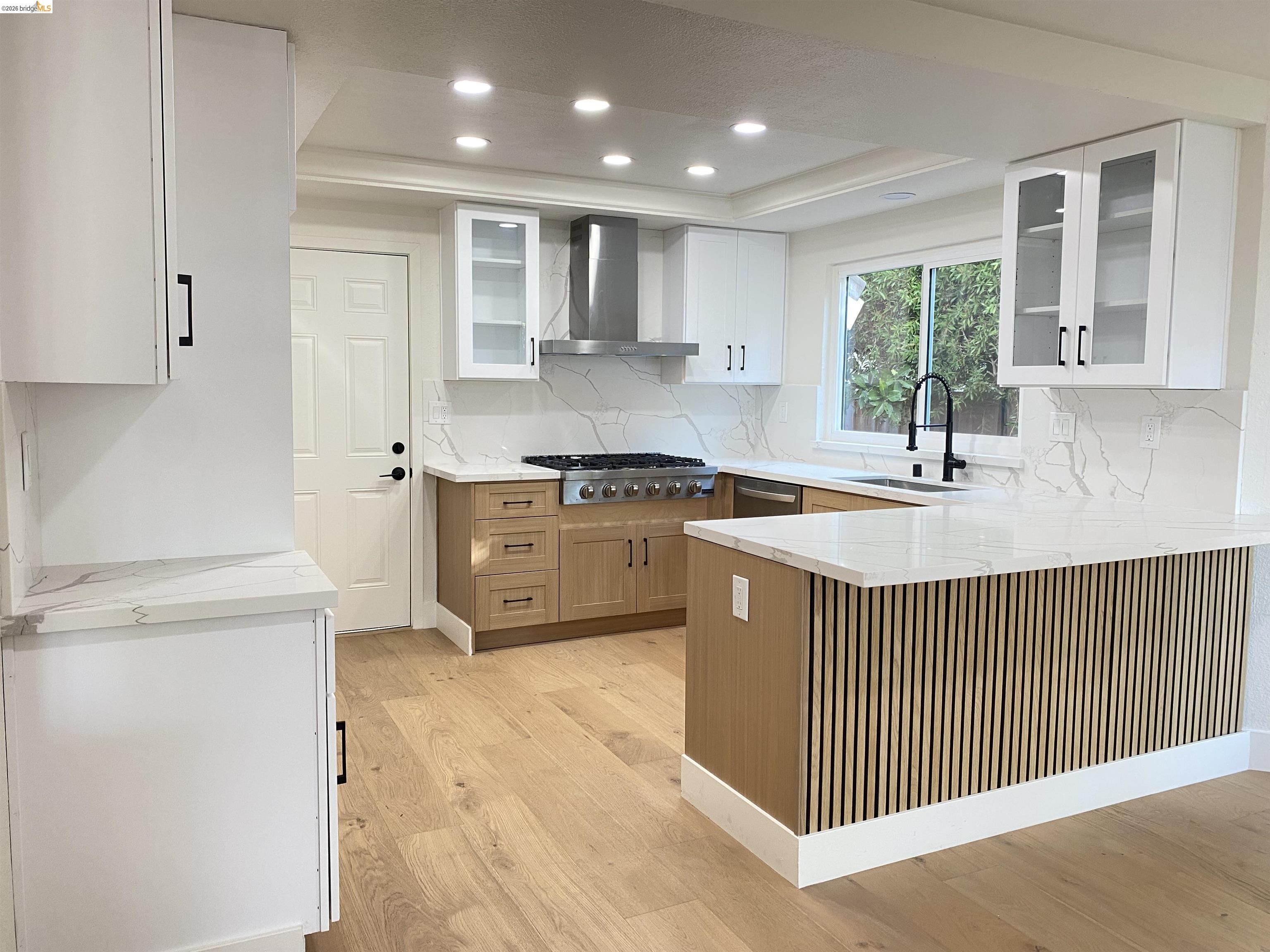 11 Paddock Court Pleasant Hill, CA 94523 - Photo 17 of 34 Kitchen featuring glass insert cabinets, light stone counters, a peninsula, white cabinetry, and wall chimney exhaust hood