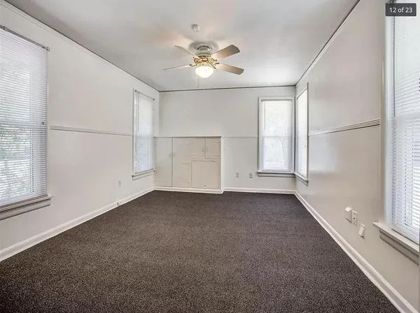 an empty room with chandelier fan and windows