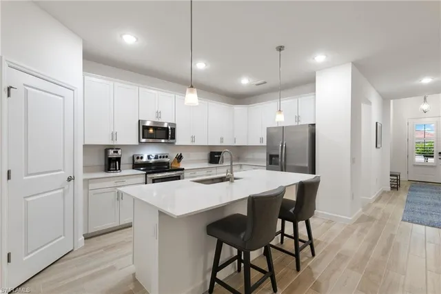 a kitchen with stainless steel appliances a stove a sink a refrigerator and white cabinets with wooden floor