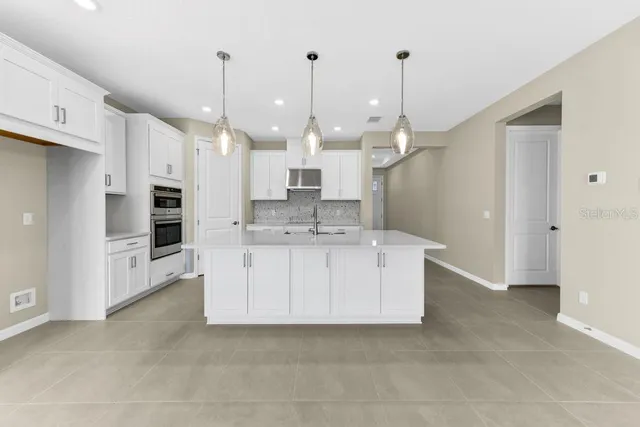 a large white kitchen with stainless steel appliances kitchen island granite countertop a refrigerator a oven a white stove with white cabinets