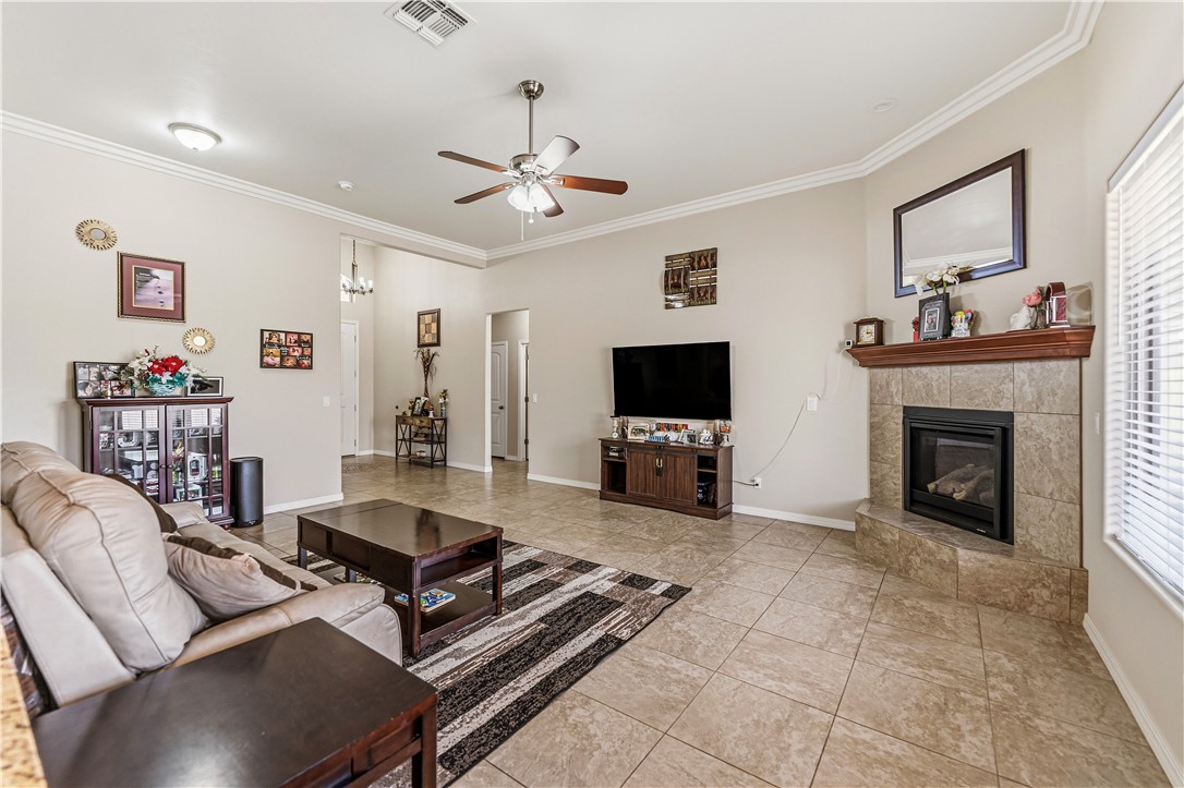 4143 North Stampede Road Kingman, AZ 86401 - Photo 10 of 42 Spacious living area featuring neutral wall tones, tile flooring, a built-in fireplace with a tile surround and wood mantel, crown molding, and a ceiling fan