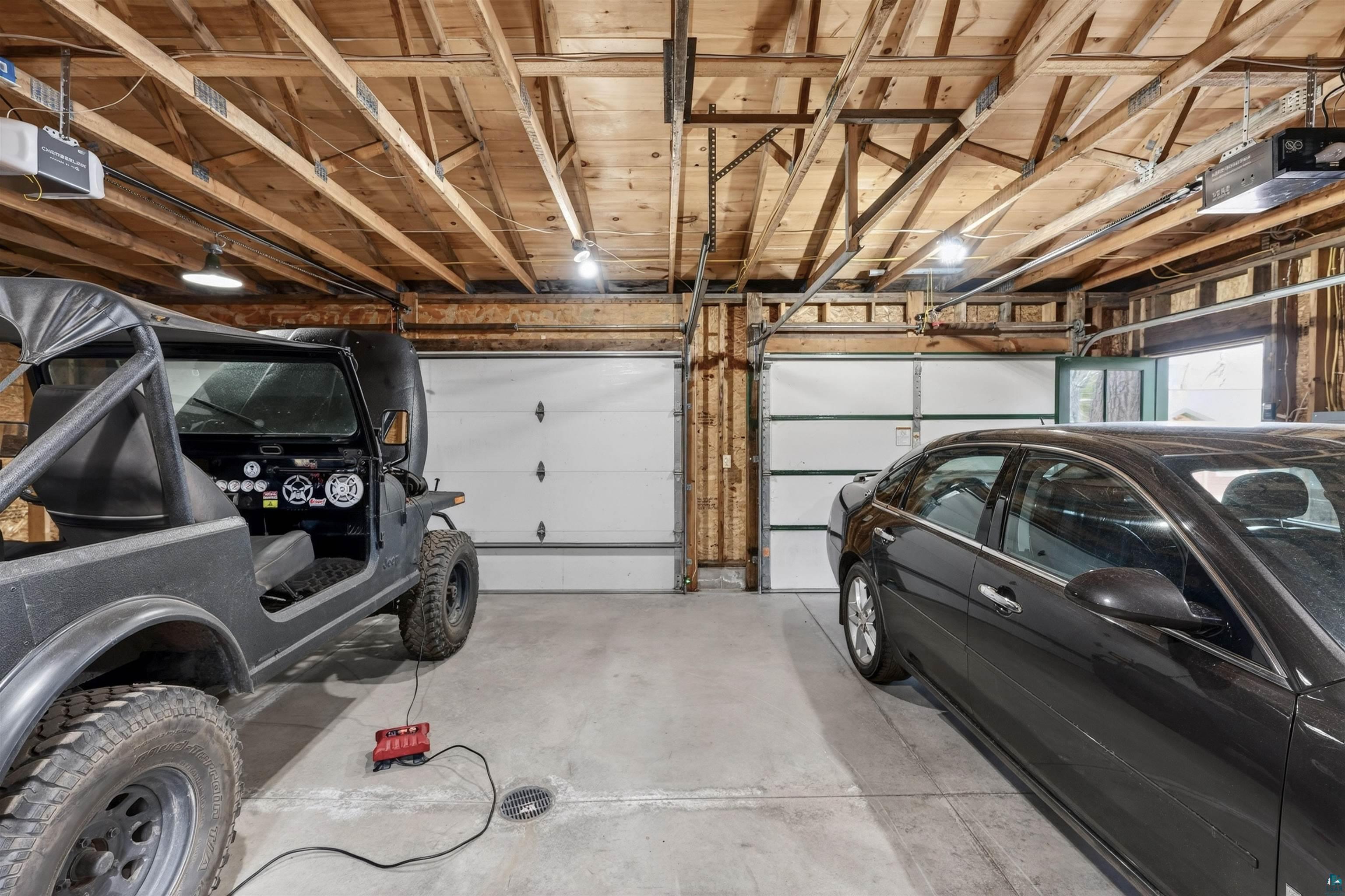 13885 Park Road Brule, WI 54820 - Photo 36 of 41 Two-car garage featuring a concrete floor, exposed wood beam ceiling, multiple overhead lights, and two white garage doors