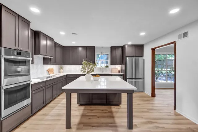 a kitchen with stainless steel appliances kitchen island granite countertop a refrigerator a sink dishwasher a stove with wooden cabinets and floor