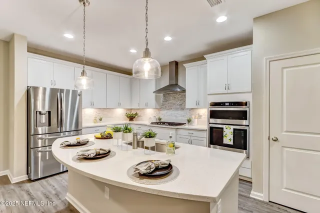 a kitchen with stainless steel appliances granite countertop a sink a stove a refrigerator and white cabinets with wooden floor