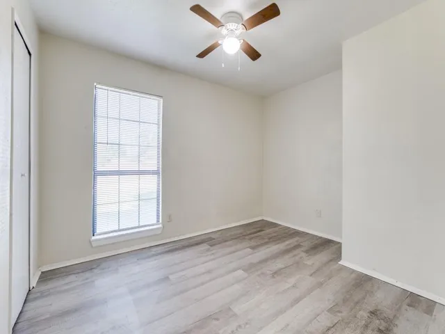 an empty room with wooden floor ceiling fan and windows
