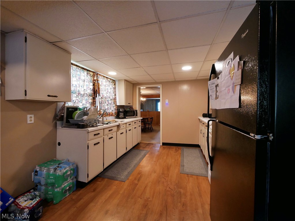 75450 Fair Road Freeport, OH 43973 - Photo 44 of 45 Kitchen with black refrigerator, a paneled ceiling, white cabinetry, and light hardwood / wood-style floors