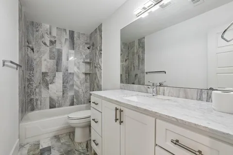 a bathroom with a granite countertop sink a toilet a mirror a bathtub and shower