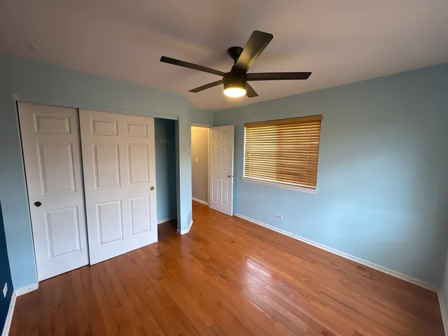 a view of an empty room with wooden floor and a ceiling fan