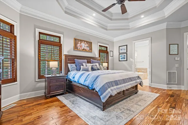 a spacious bedroom with a bed painting on wall and two windows