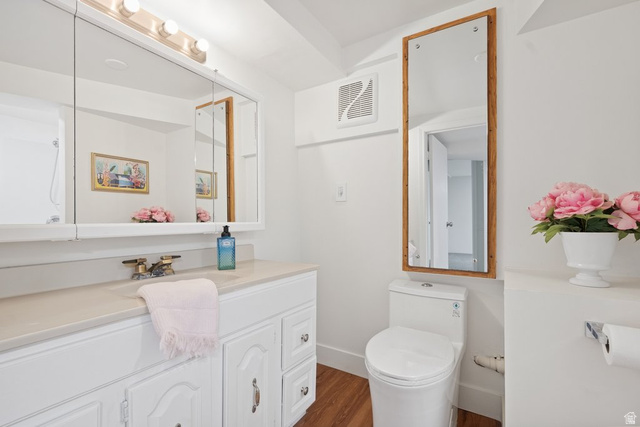 673 East 700 South Springville, UT 84663 - Photo 33 of 43 Bathroom featuring a white vanity with integrated sink, a medicine cabinet with mirrored doors, a wall-mounted full-length mirror with a wood frame, a white toilet, and wood-finish flooring