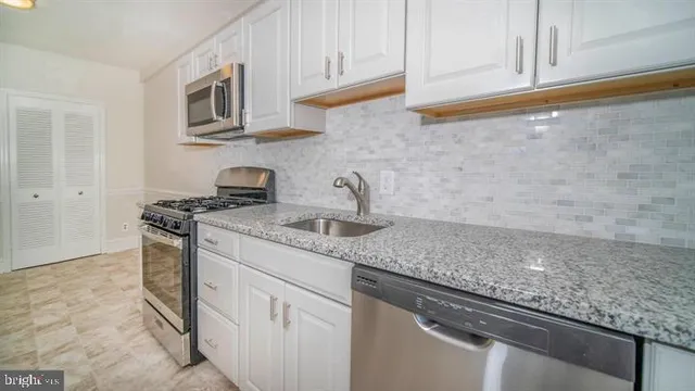 a kitchen with stainless steel appliances granite countertop white cabinets and a stove top oven
