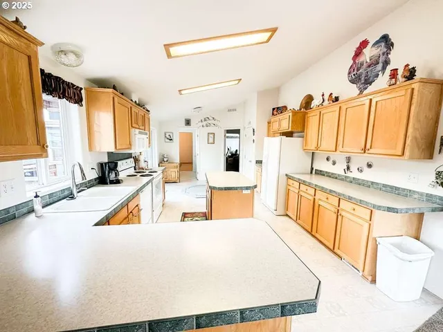 a large white kitchen with stainless steel appliances a stove a sink a refrigerator and a white cabinets next to a window