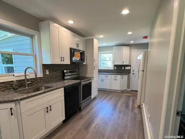 a kitchen with stainless steel appliances granite countertop a refrigerator a sink dishwasher a stove and white cabinets with wooden floor