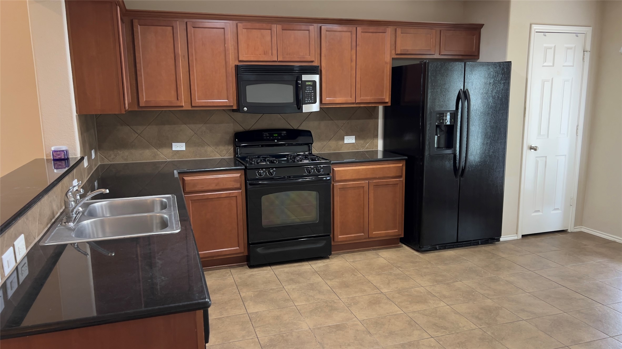 357 Nottingham Loop Kyle, TX 78640 - Photo 4 of 22 Rich wood cabinetry paired with dark stone countertops defines this functional kitchen space.