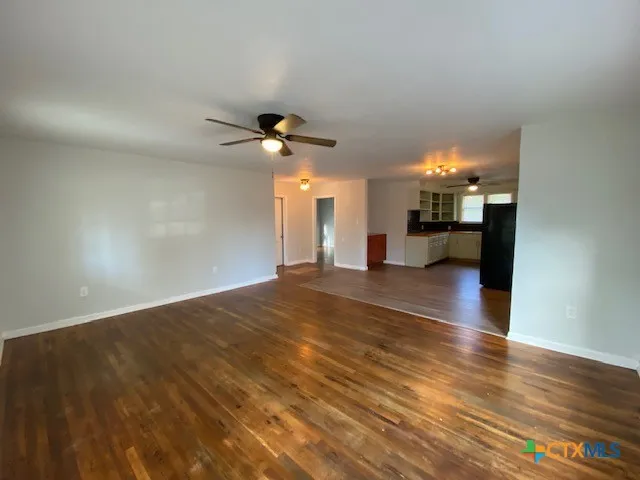 a view of an empty room and kitchen with wooden floor