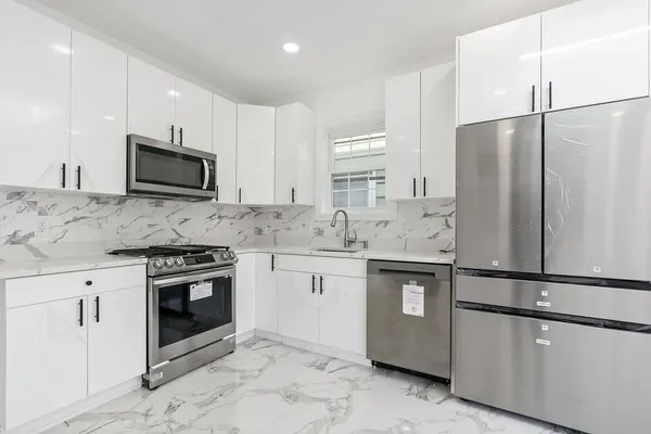 a kitchen with stainless steel appliances granite countertop a refrigerator stove a sink and white cabinets